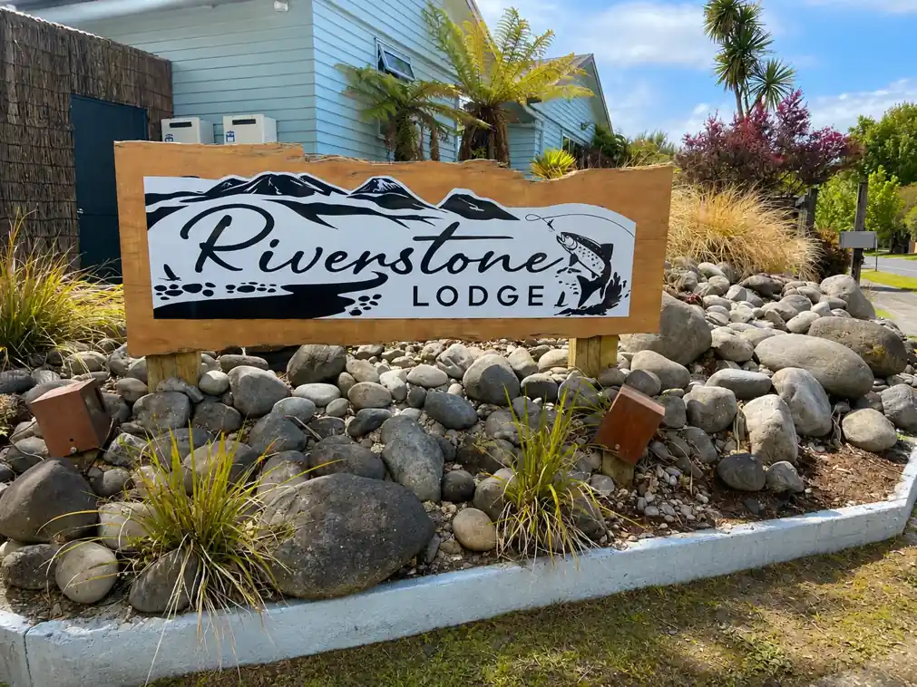 Riverstone Lodge sign set among river stones at the entrance in Tūrangi
